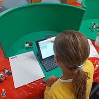 Kind arbeitet mit Playmobil Figuren an einer Greenscreen