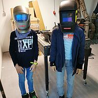 zwei Kinder mit Schweißerhelmen auf dem Kopf