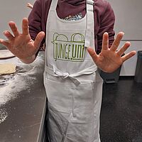 Kind trägt JUBoh Schürze und streckt seine bemehlten Hände in die Kamera